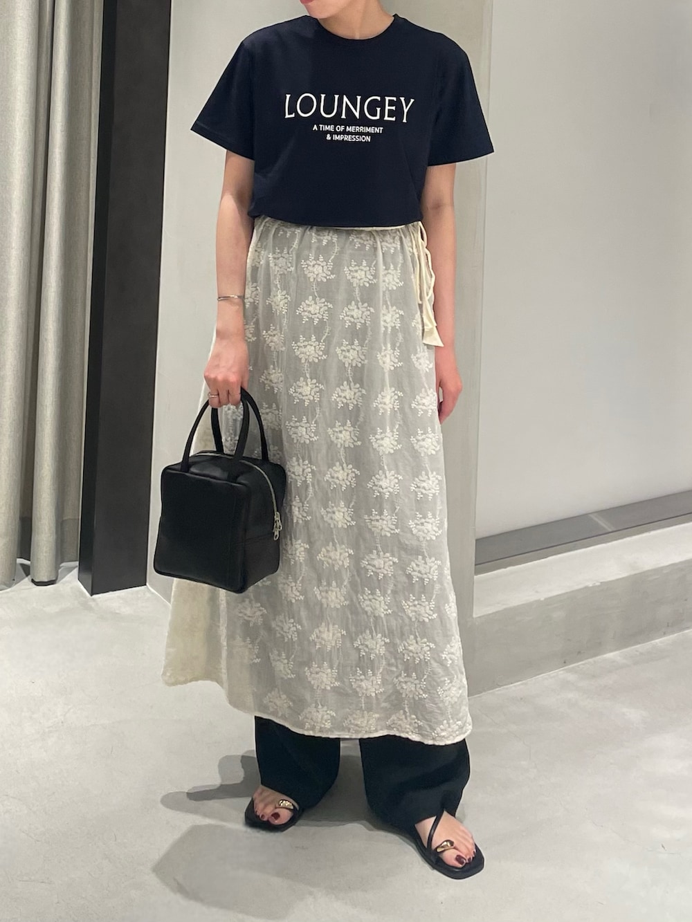 ブラック系のボストンバッグ、ブルー系のTシャツ/カットソー、ホワイト系のスカートを着用したレディースの夏コーディネートの2枚目の写真