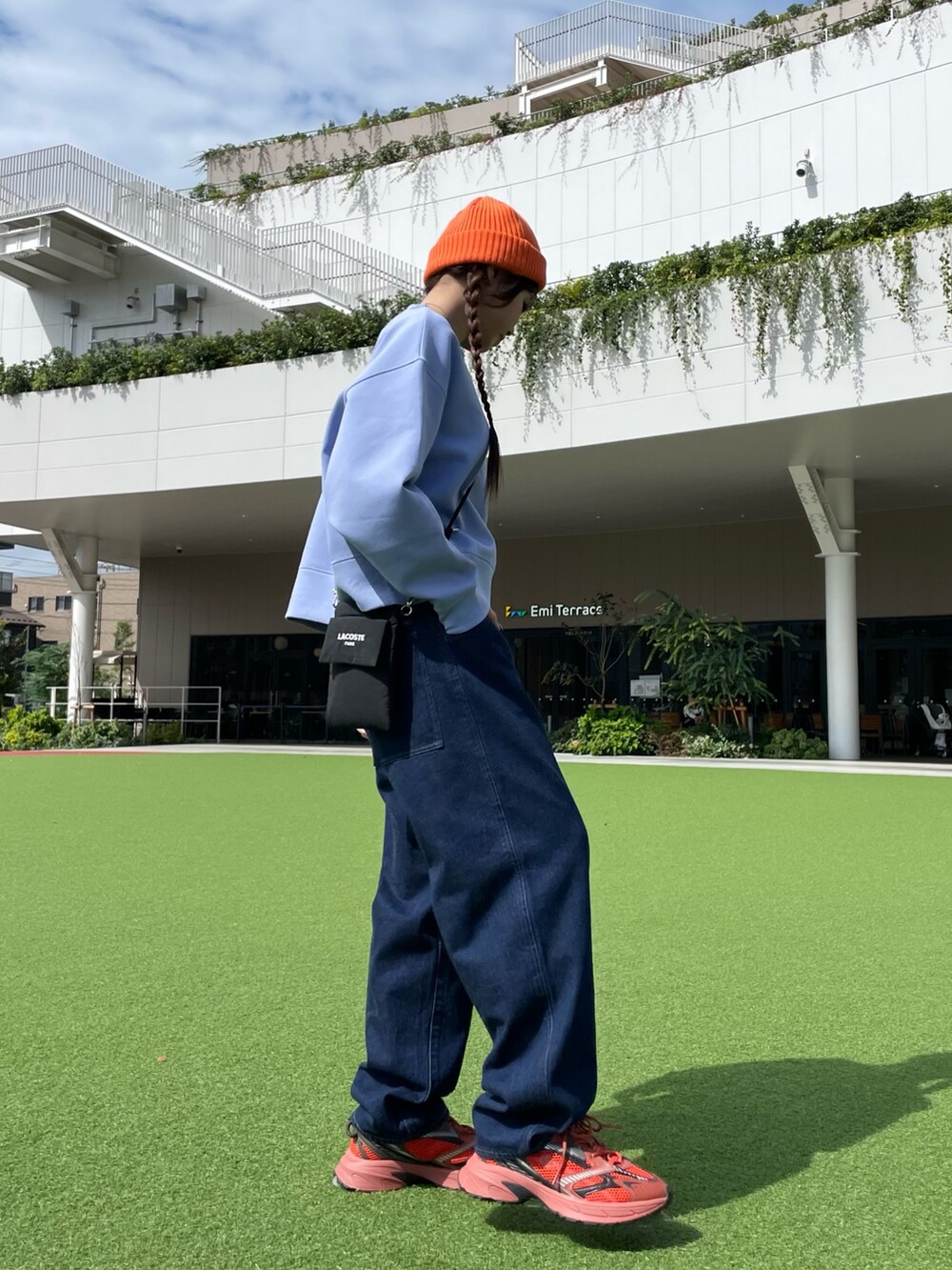 レッド系のスニーカー、ブラック系のショルダーバッグ、ブルー系のデニムパンツを着用したレディースの秋コーディネートの4枚目の写真