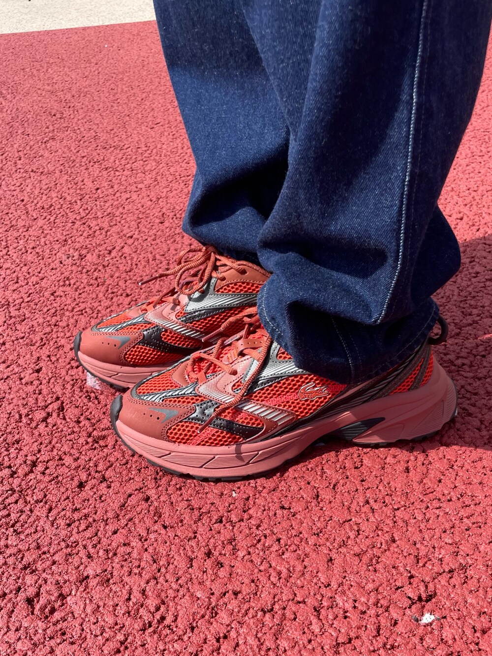 レッド系のスニーカー、ブラック系のショルダーバッグ、ブルー系のデニムパンツを着用したレディースの秋コーディネートの6枚目の写真