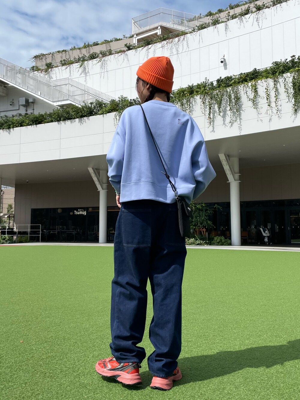 レッド系のスニーカー、ブラック系のショルダーバッグ、ブルー系のデニムパンツを着用したレディースの秋コーディネートの5枚目の写真