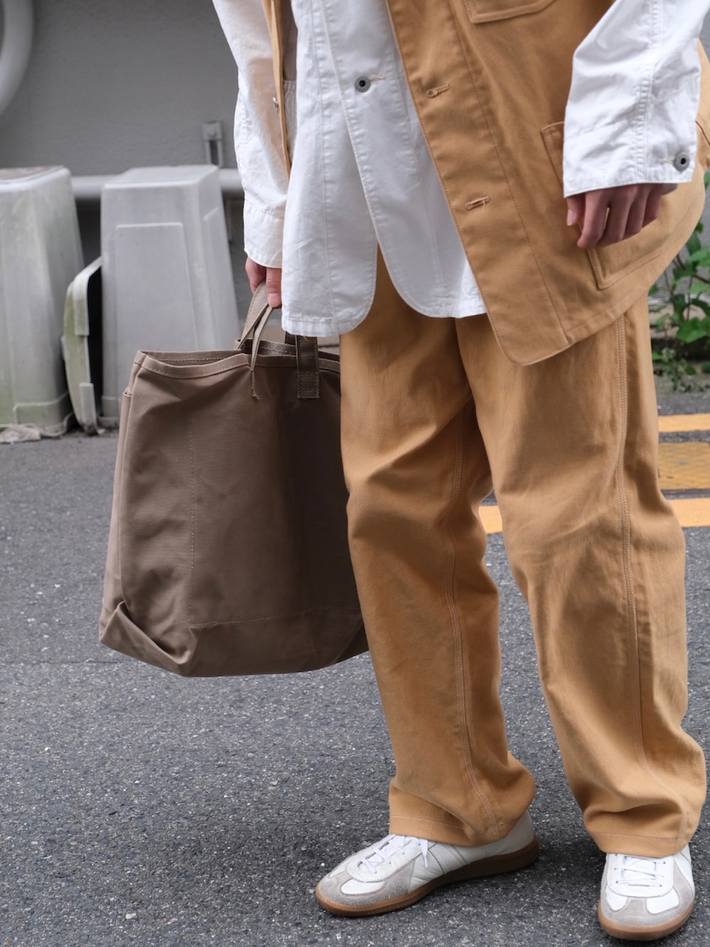 ベージュ系のトートバッグ、ホワイト系のスニーカー、ベージュ系のベストを着用したメンズの春コーディネートの2枚目の写真