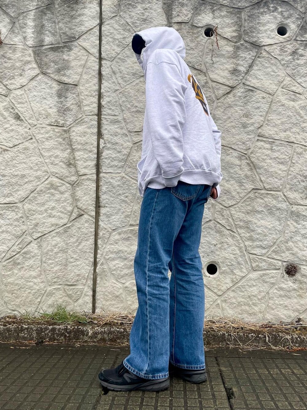 グレー系のパーカー、ブルー系のデニムパンツ、ブラック系のスニーカーを着用したメンズの春コーディネートの2枚目の写真