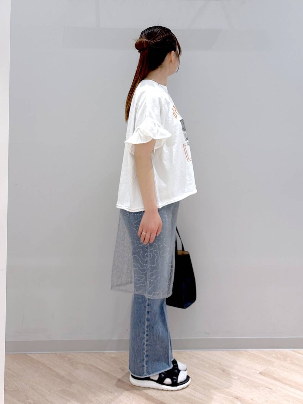 ブルー系のデニムパンツ、ホワイト系のショルダーバッグ、ブラック系のサンダルを着用したレディースの春コーディネートの3枚目の写真