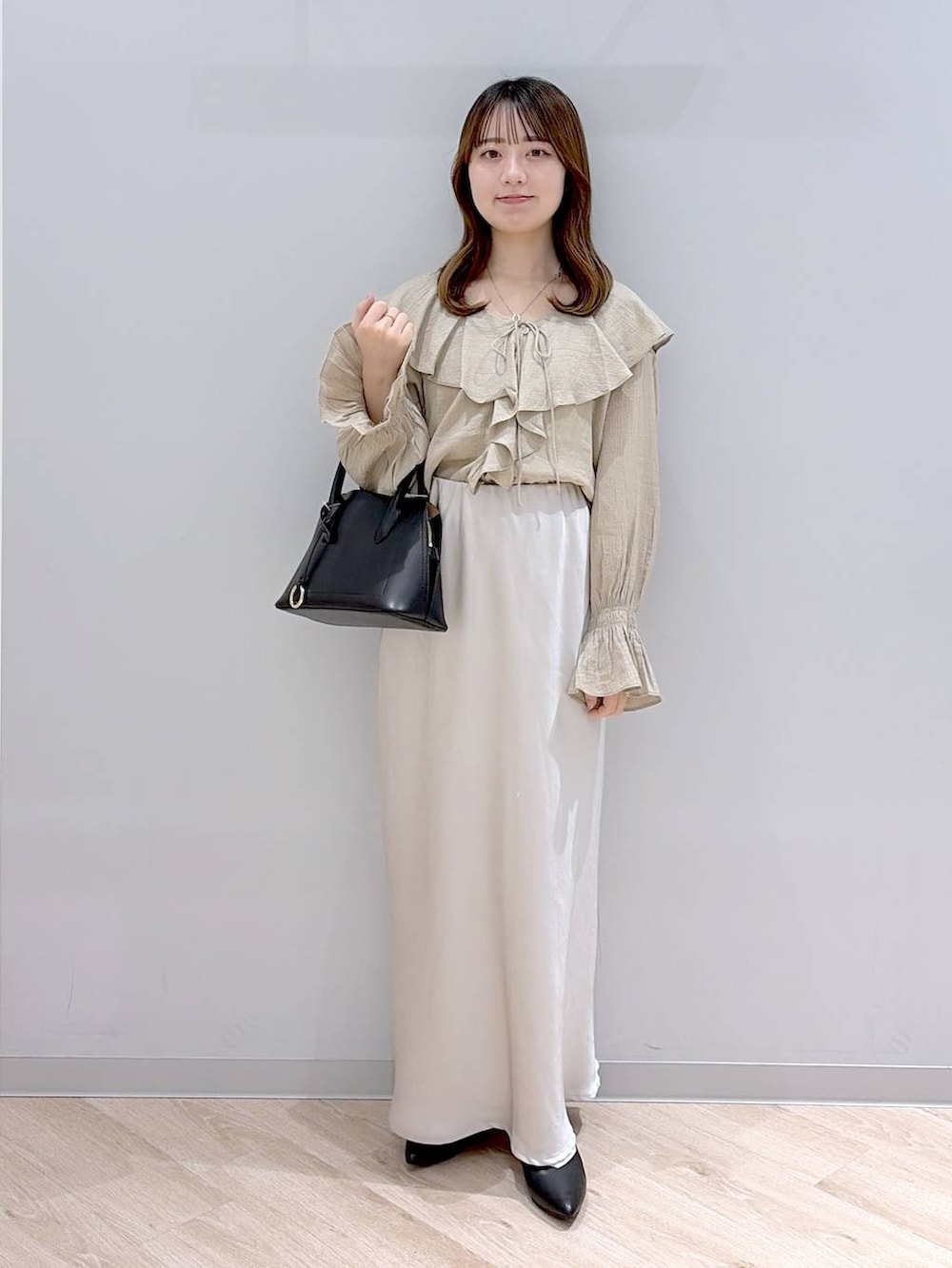 ブラック系のショルダーバッグ、ブラック系のパンプス、グレー系のスカートを着用したレディースの春コーディネートの2枚目の写真