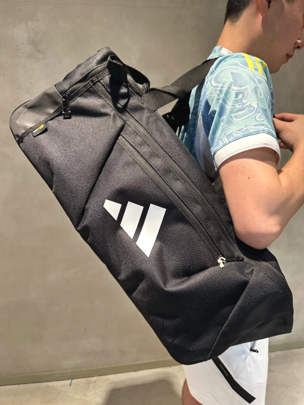 ブルー系のトップス、ホワイト系のシューズ、ブラック系のボストンバッグを着用したメンズの夏コーディネートの2枚目の写真