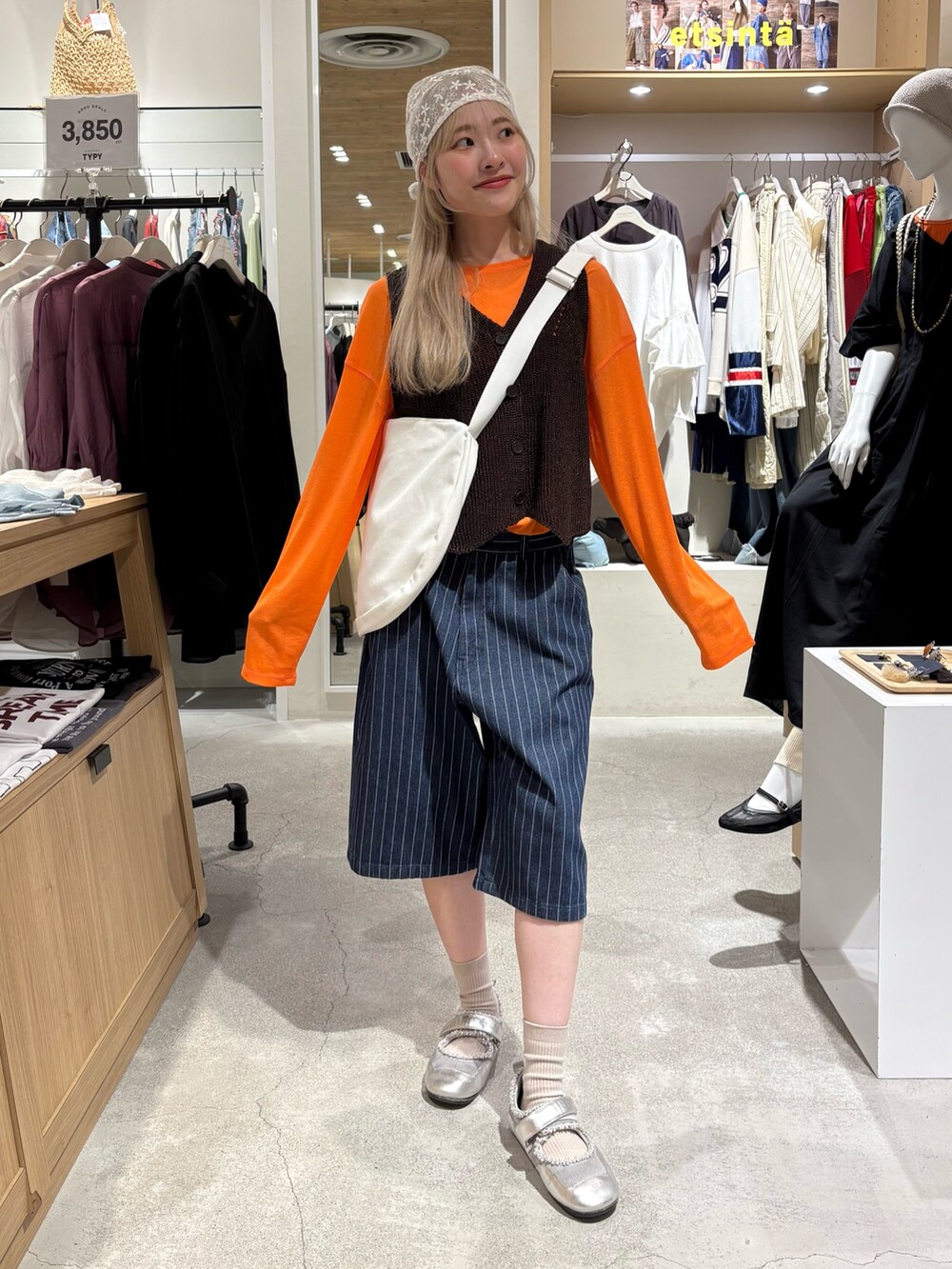 オレンジ系のTシャツ/カットソー、ブラウン系のベスト、ホワイト系のショルダーバッグを着用したレディースの夏コーディネートの4枚目の写真