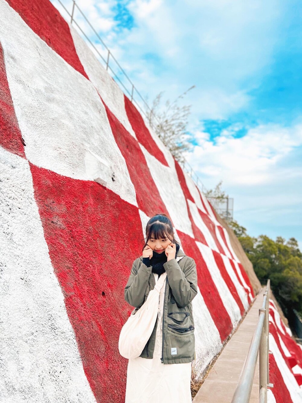 グリーン系のライダースジャケット、ベージュ系のハンドバッグ、ベージュ系のワンピース/ドレスを着用したレディースの夏コーディネートの2枚目の写真