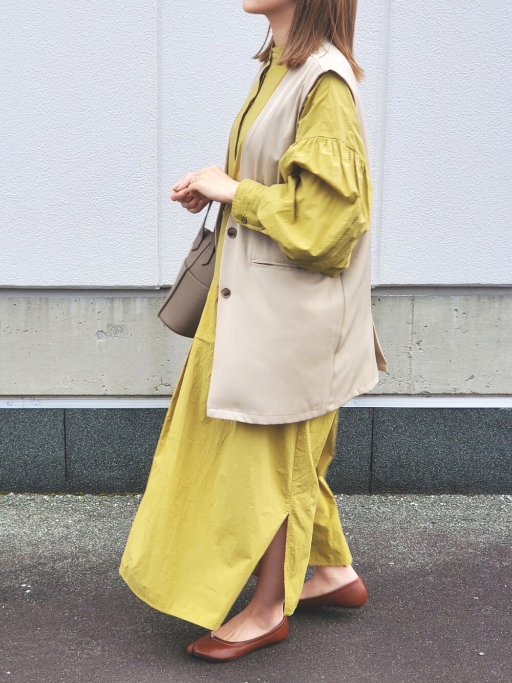 ベージュ系のベスト、グリーン系のワンピース、ブラウン系のハンドバッグを着用したレディースの春コーディネートの2枚目の写真