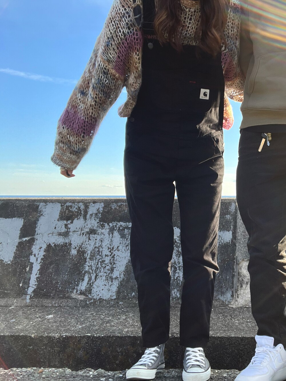 グレー系のスニーカー、ブラック系のサロペット/オーバーオール、ベージュ系のニット/セーターを着用したレディースの春コーディネートの2枚目の写真