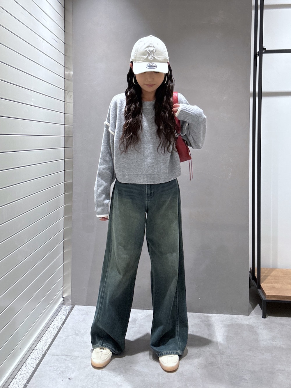 ブルー系のデニムパンツ、グレー系のニット/セーター、レッド系のショルダーバッグを着用したレディースの秋コーディネートの2枚目の写真
