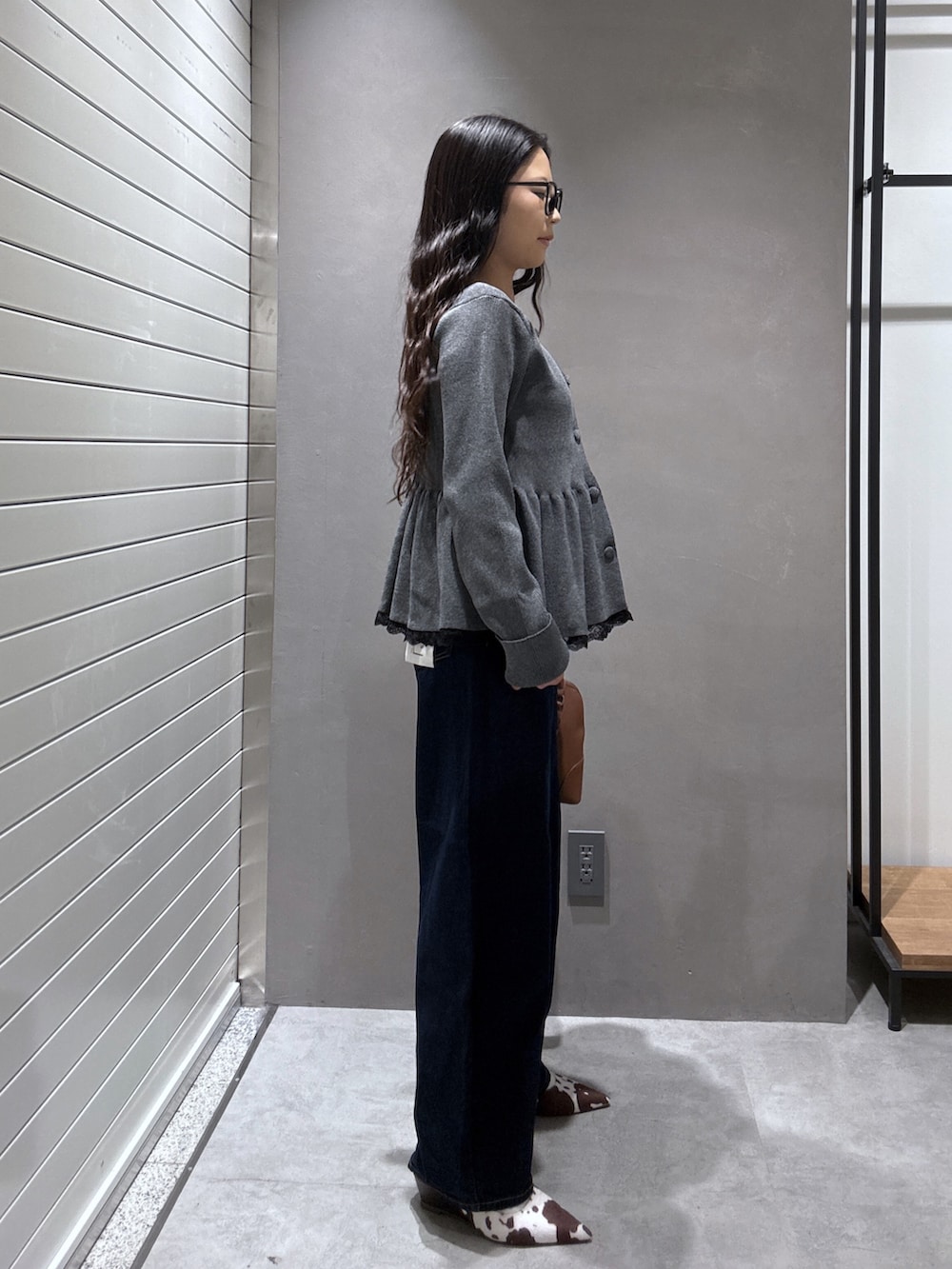 グレー系のニット/セーター、ブラウン系のショルダーバッグ、ブルー系のデニムパンツを着用したレディースの秋コーディネートの2枚目の写真