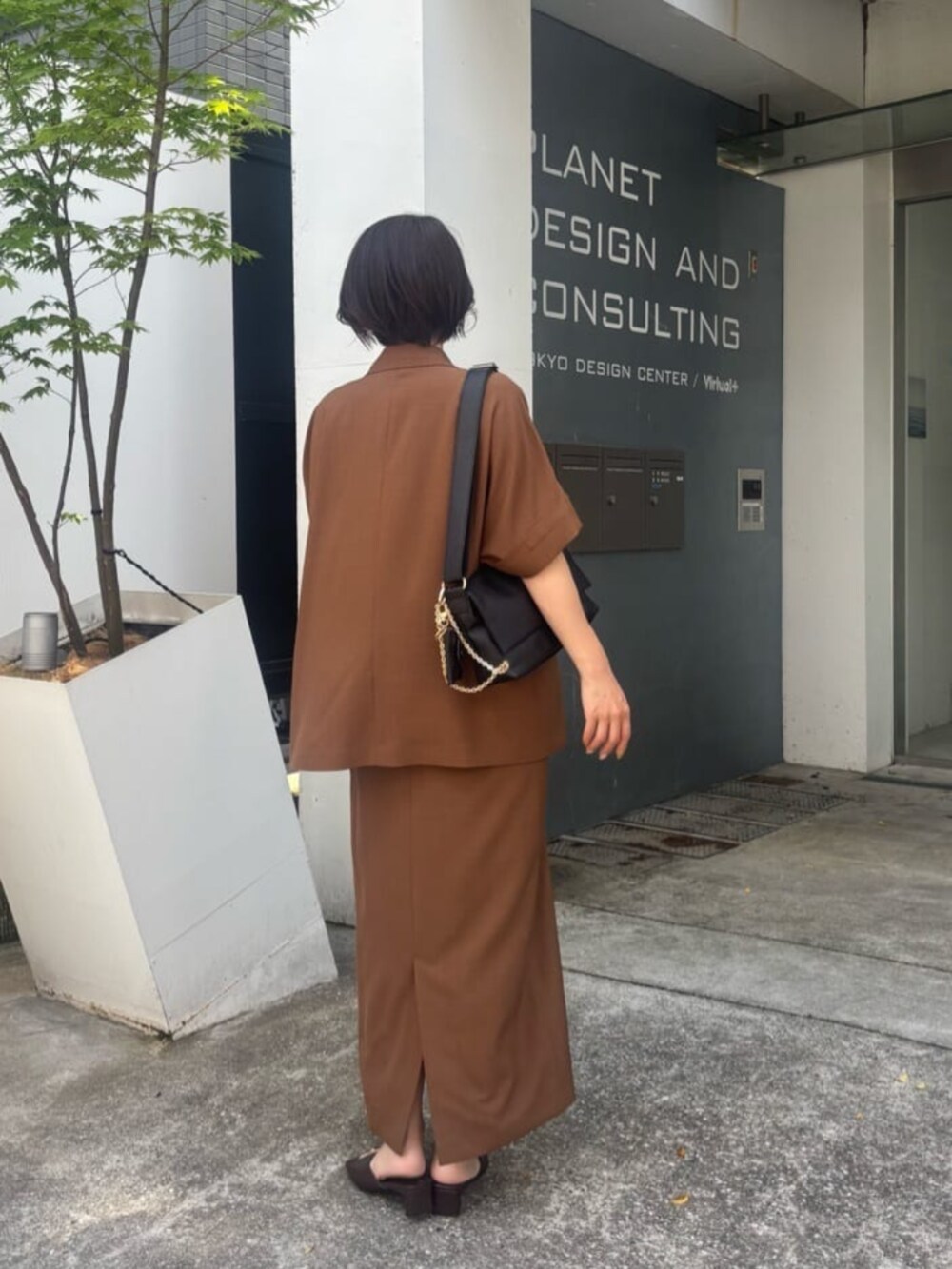 ブラック系のショルダーバッグ、ブラウン系のワンピースを着用したレディースの夏コーディネートの2枚目の写真