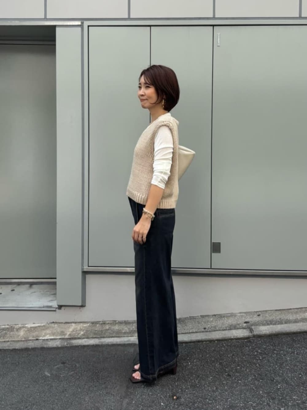 ホワイト系のショルダーバッグ、ベージュ系のベスト、ブルー系のデニムパンツを着用したレディースの夏コーディネートの2枚目の写真