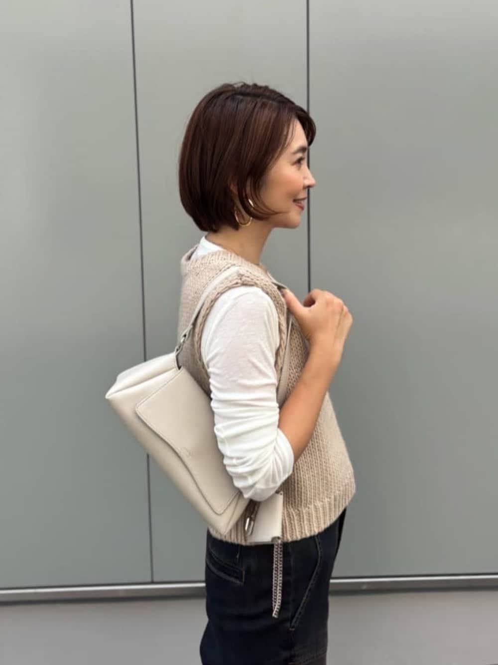 ホワイト系のショルダーバッグ、ベージュ系のベスト、ブルー系のデニムパンツを着用したレディースの夏コーディネートの4枚目の写真
