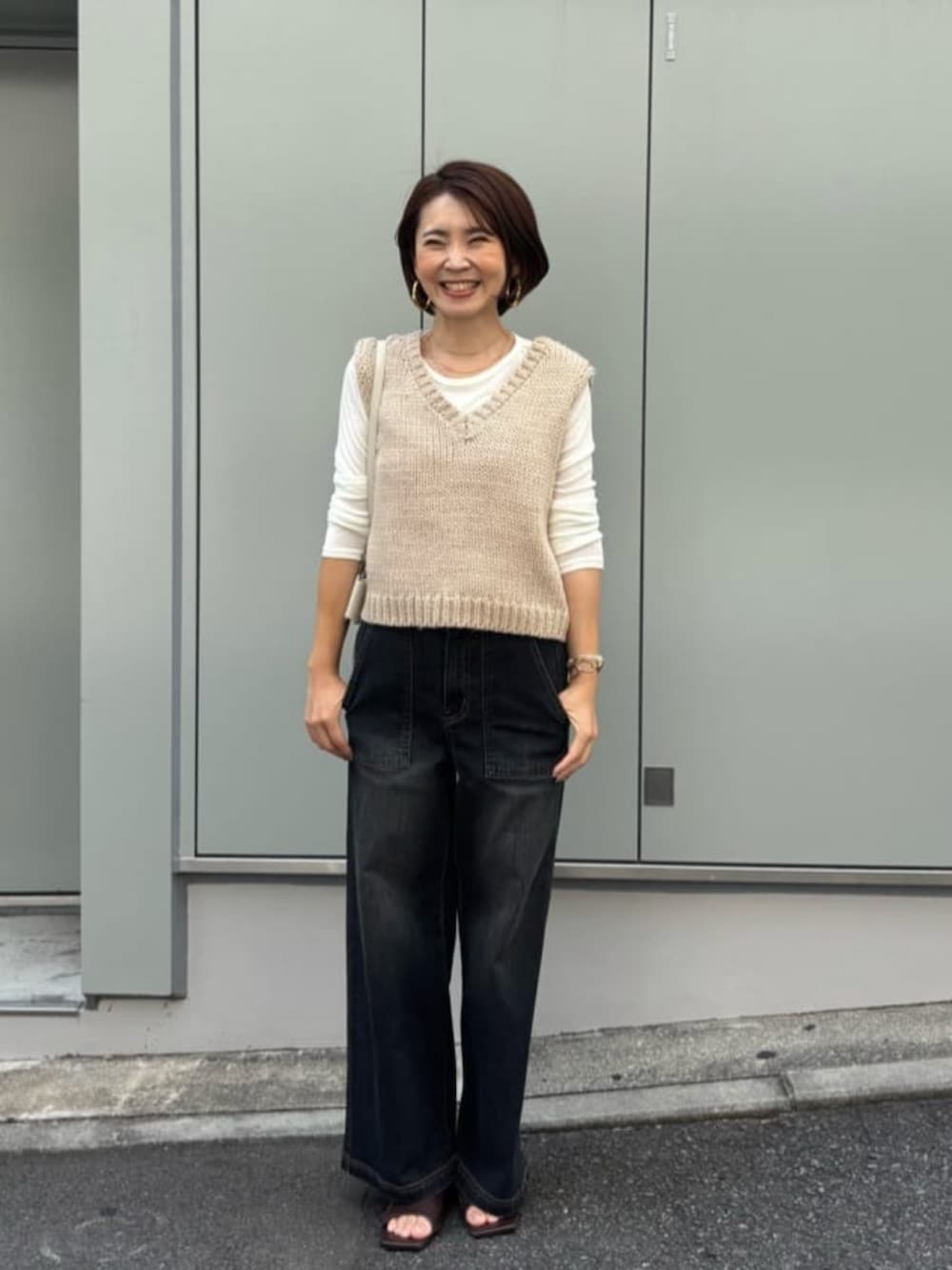 ホワイト系のショルダーバッグ、ベージュ系のベスト、ブルー系のデニムパンツを着用したレディースの夏コーディネートの3枚目の写真