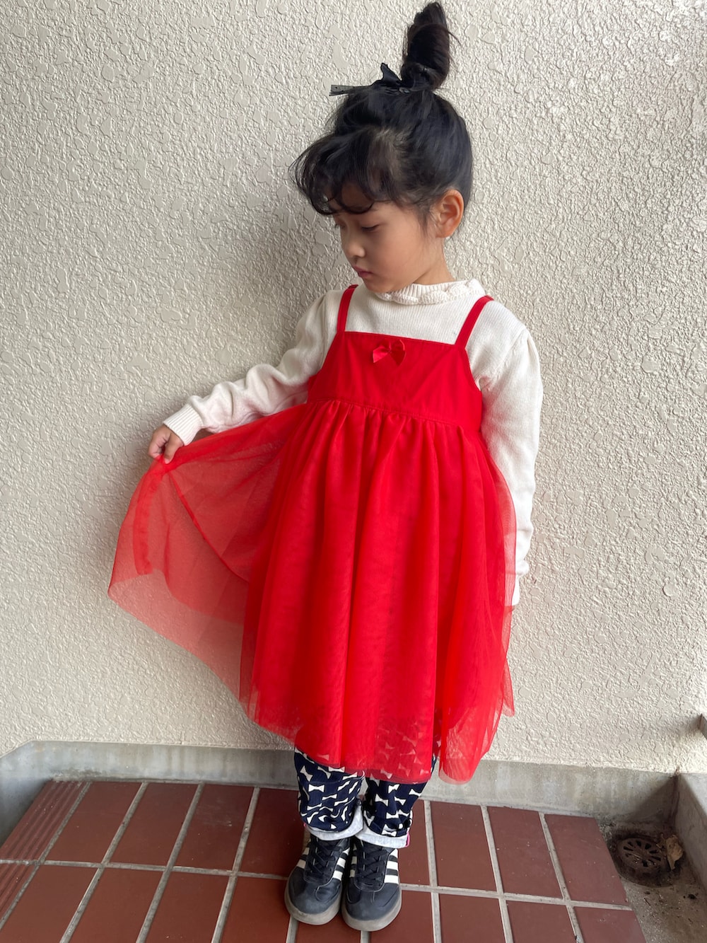 レッド系のチュニック、ブルー系のデニムパンツ、ブラック系のスニーカーを着用したキッズの冬コーディネートの3枚目の写真