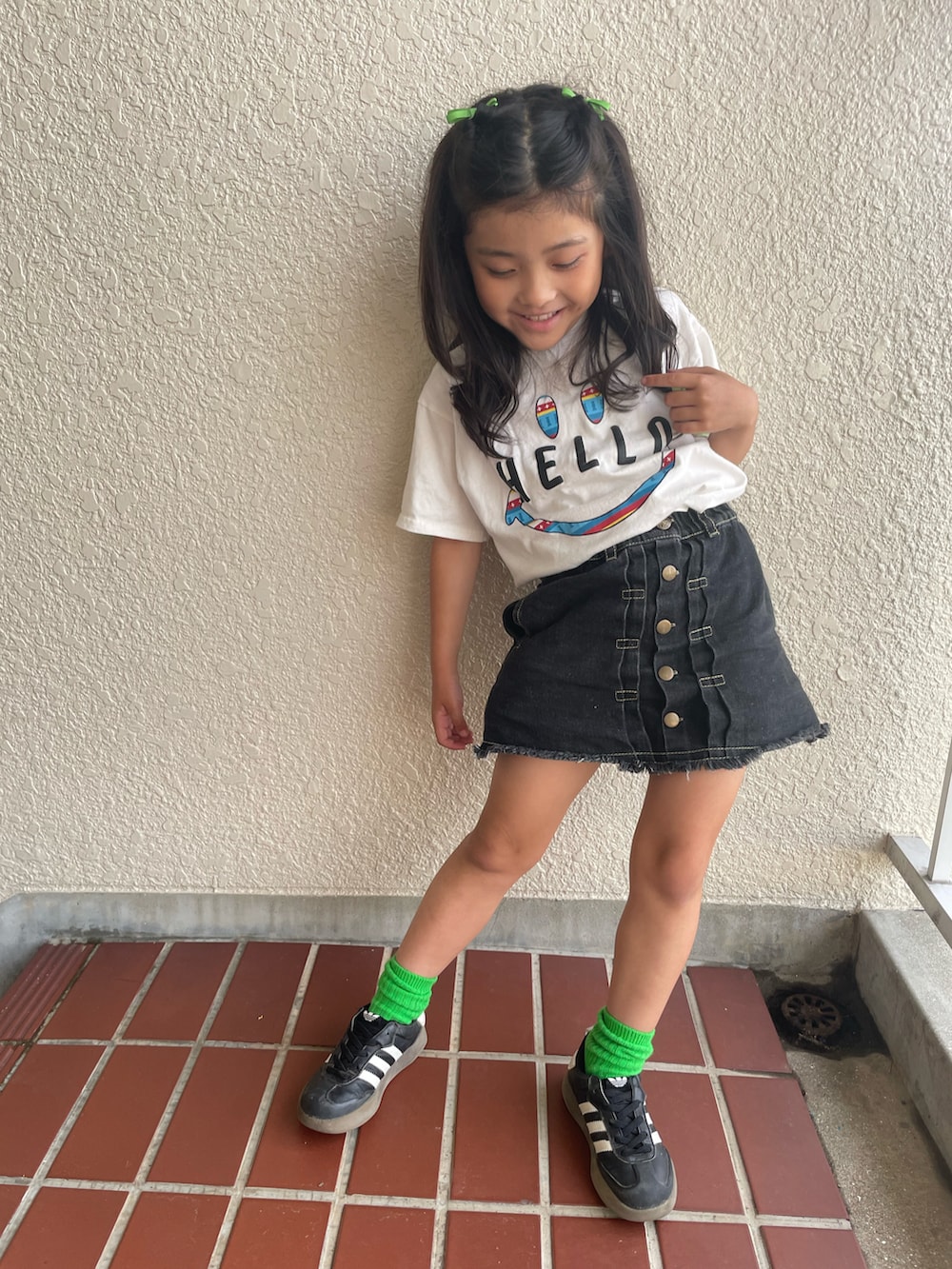 ブラック系のデニムスカート、ホワイト系のTシャツ/カットソー、ブラック系のスニーカーを着用したキッズの夏コーディネートの2枚目の写真