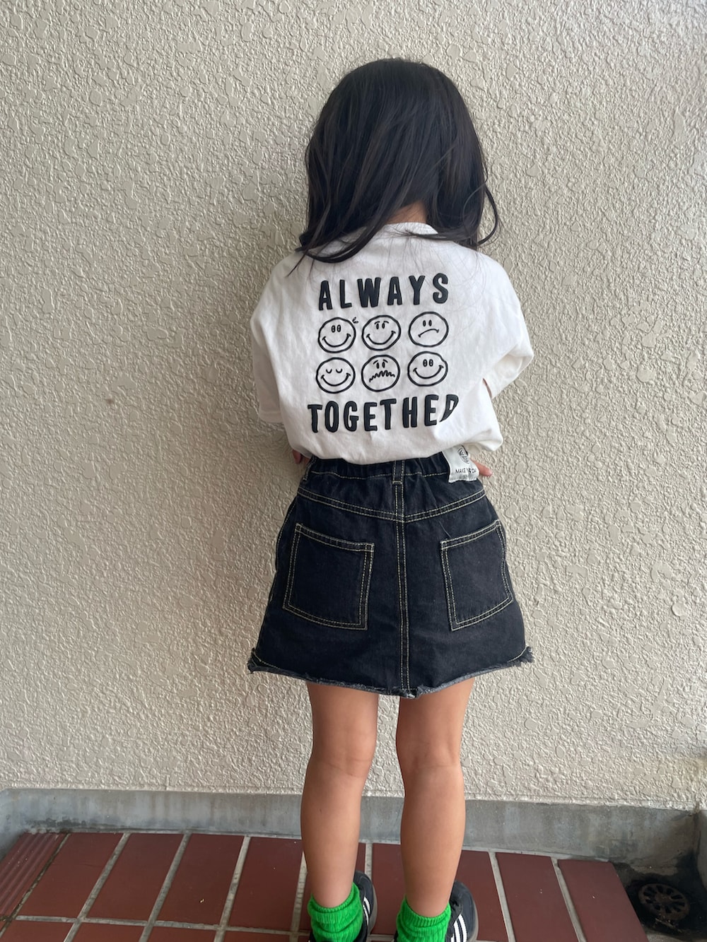 ブラック系のデニムスカート、ホワイト系のTシャツ/カットソー、ブラック系のスニーカーを着用したキッズの夏コーディネートの3枚目の写真
