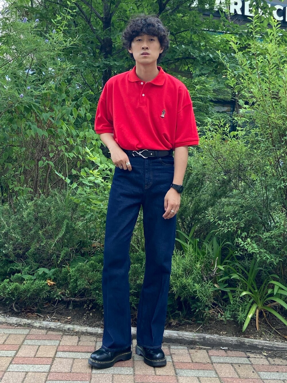 レッド系のポロシャツ、ブルー系のデニムパンツ、ブラック系のシューズを着用したメンズの夏コーディネートの2枚目の写真