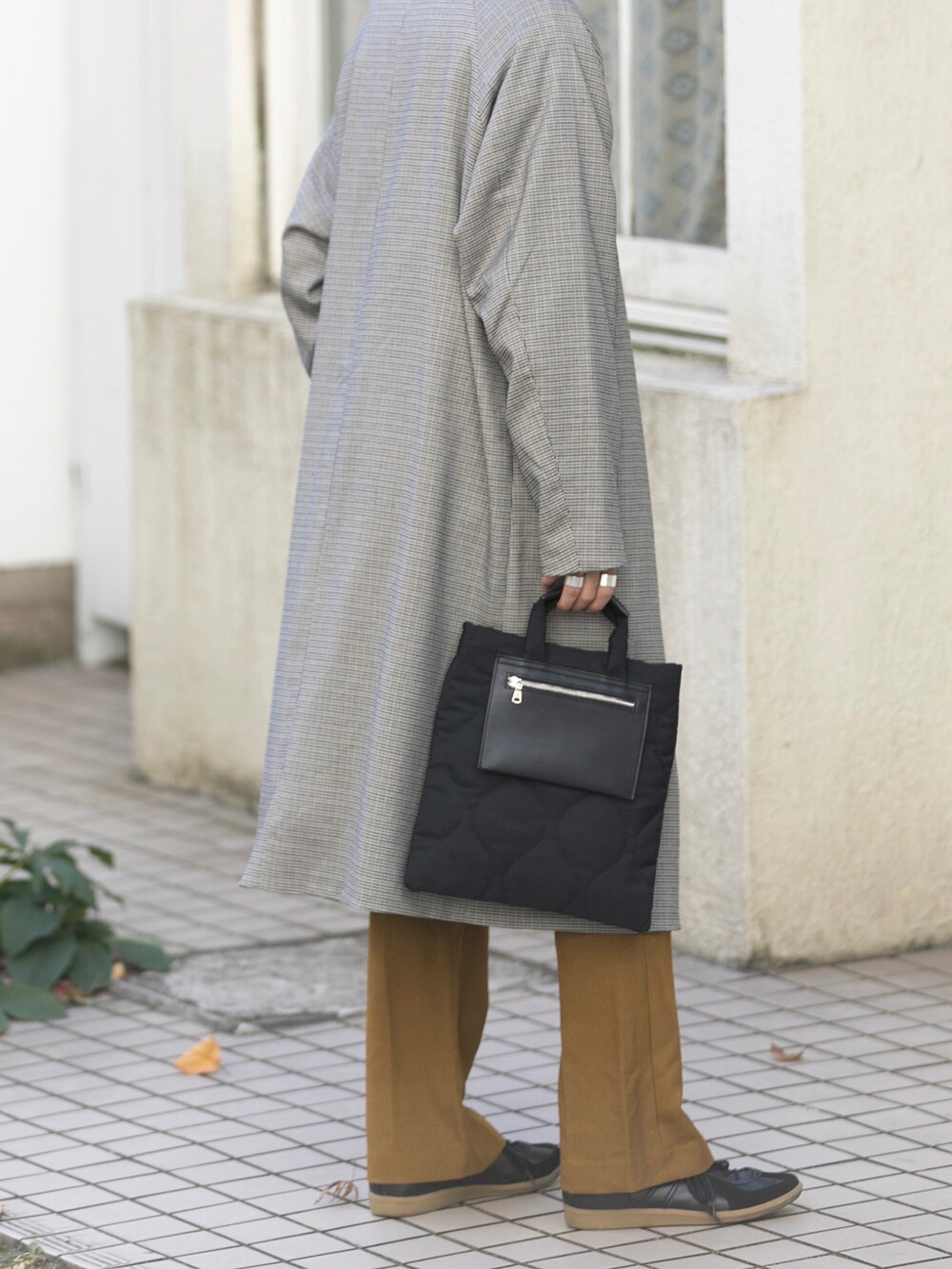 ブラック系のトートバッグ、ベージュ系のステンカラーコート、ブラック系のスニーカーを着用したメンズの冬コーディネートの3枚目の写真