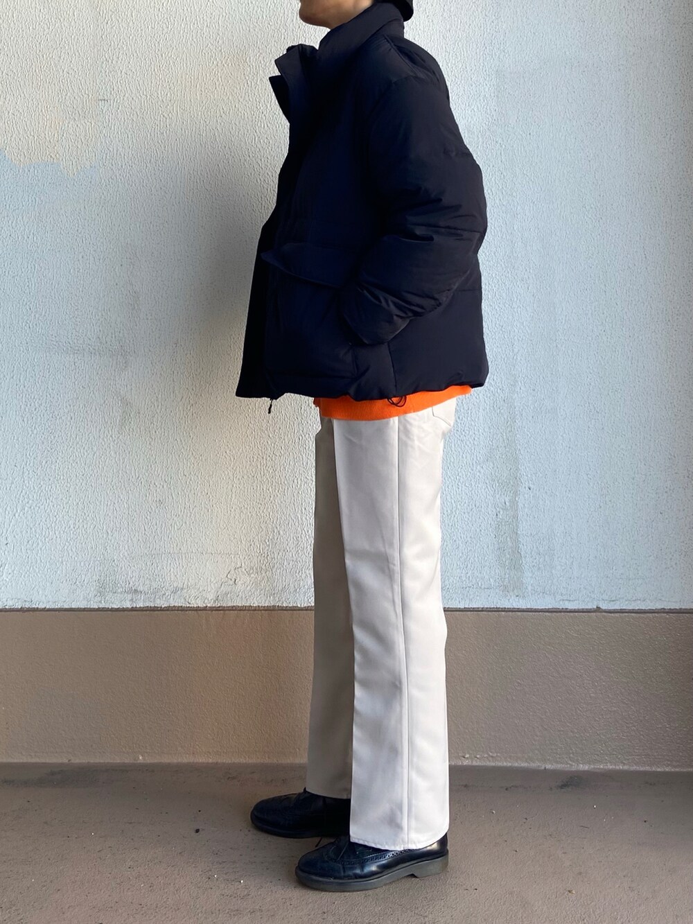 オレンジ系のカーディガン/ボレロ、ブラック系のダウンジャケット/コート、ベージュ系のスラックスを着用したメンズの冬コーディネートの2枚目の写真