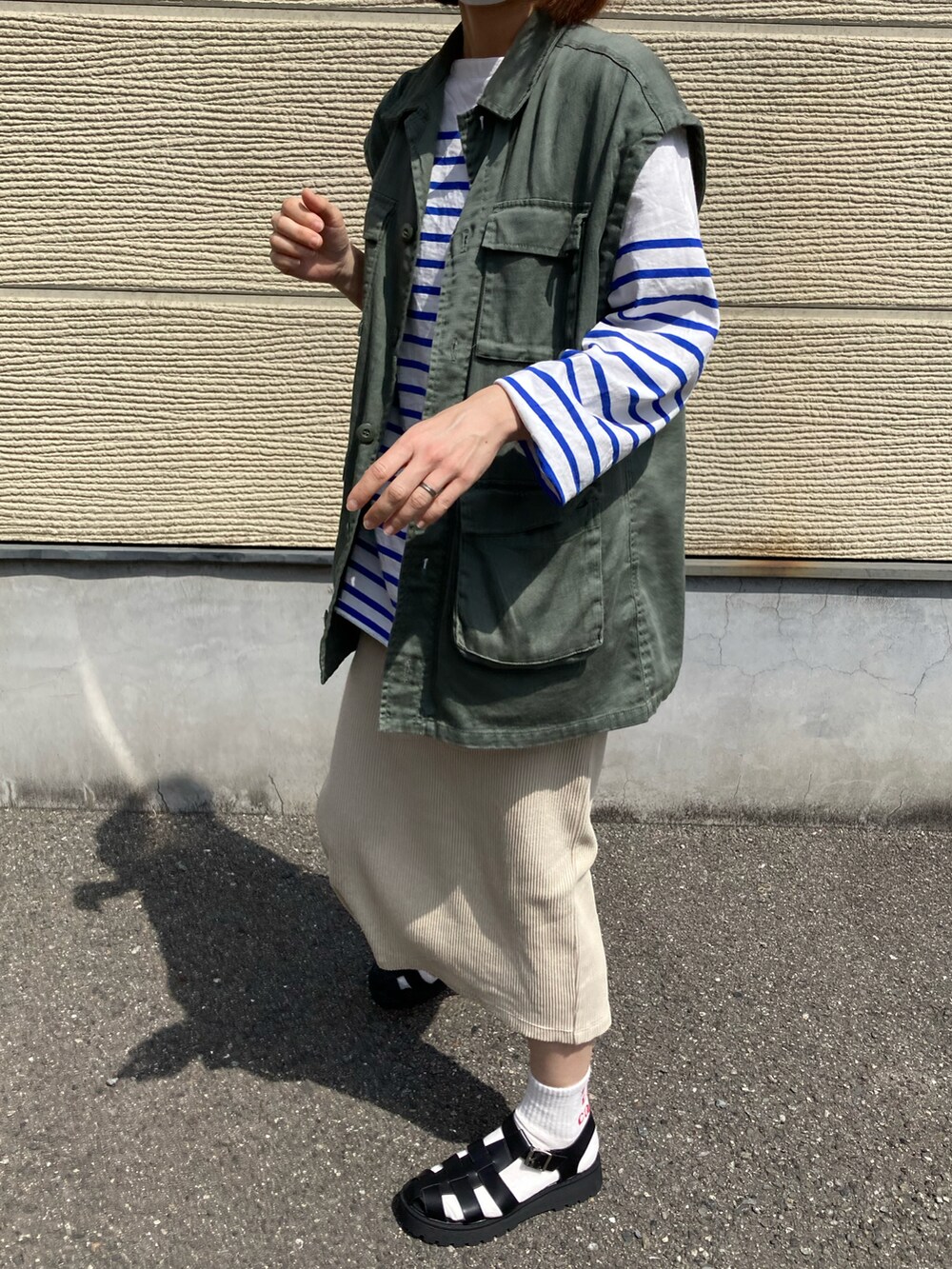 グリーン系のベスト、ブラック系のショルダーバッグ、ブラック系のサンダルを着用したレディースの春コーディネートの2枚目の写真