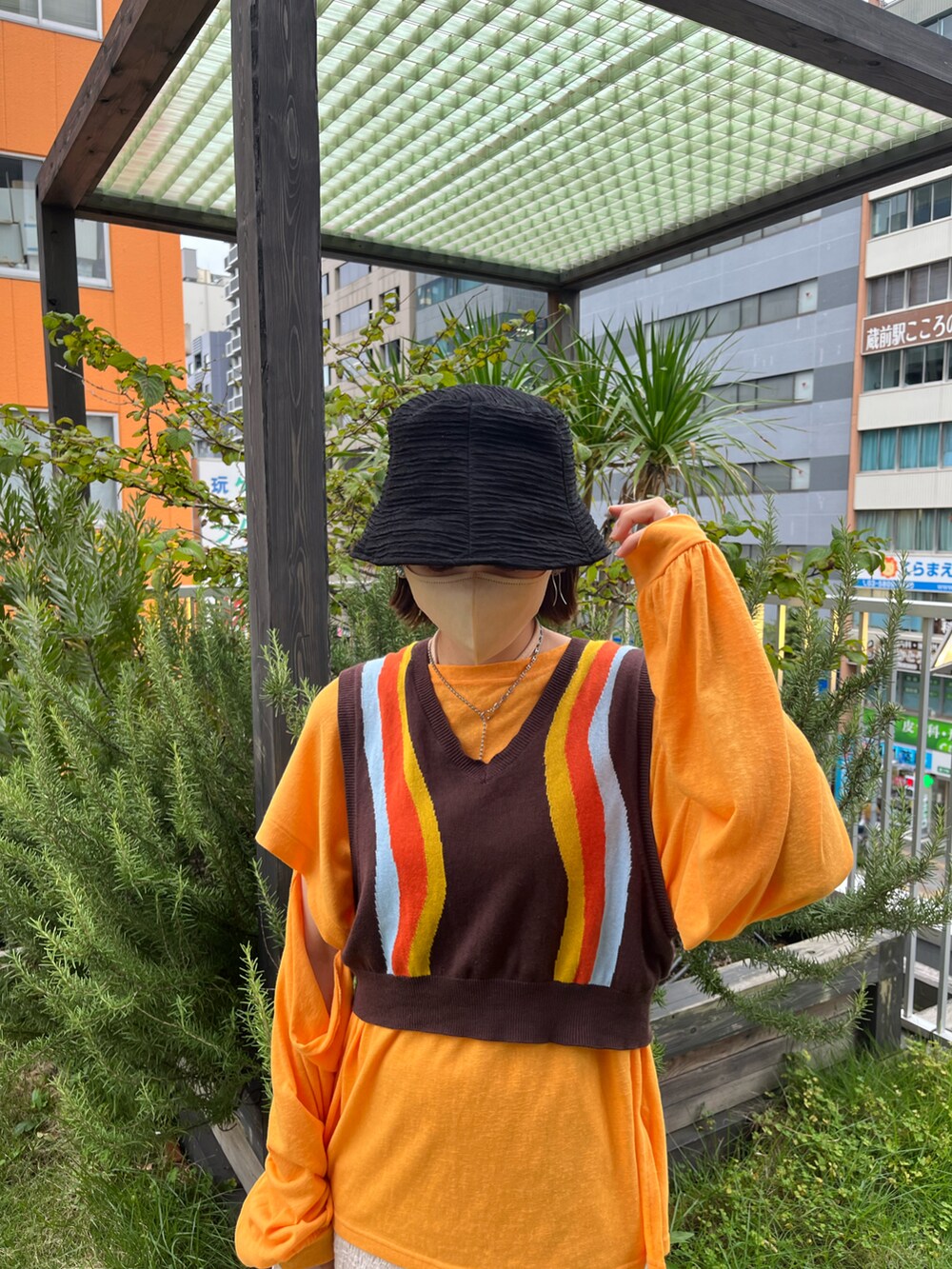 オレンジ系のTシャツ/カットソー、ブラウン系のベスト、ホワイト系のスカートを着用したレディースの夏コーディネートの3枚目の写真