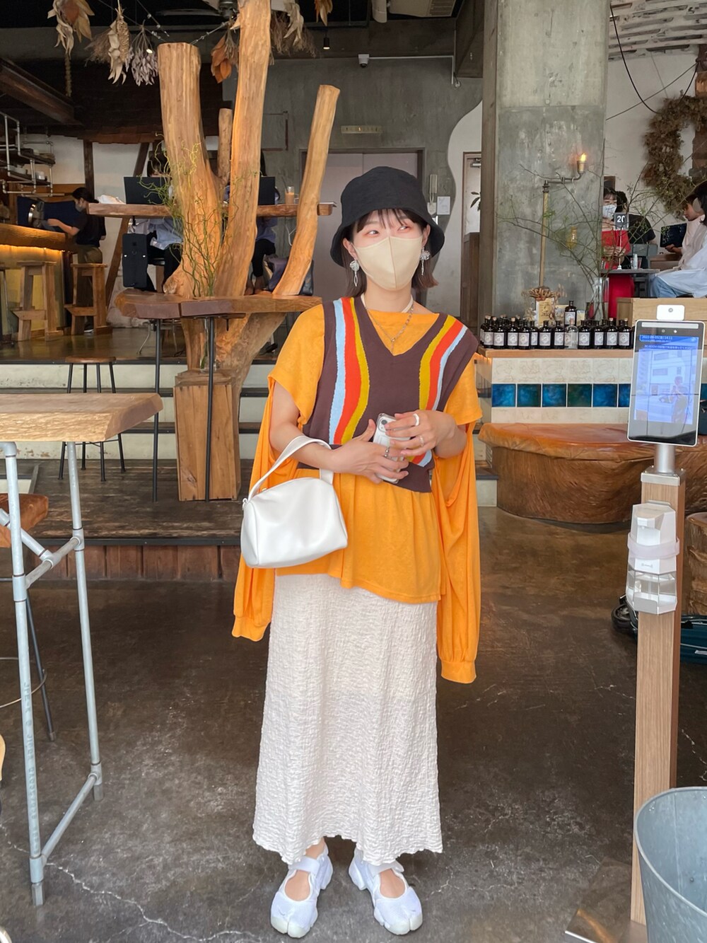 オレンジ系のTシャツ/カットソー、ブラウン系のベスト、ホワイト系のスカートを着用したレディースの夏コーディネートの2枚目の写真