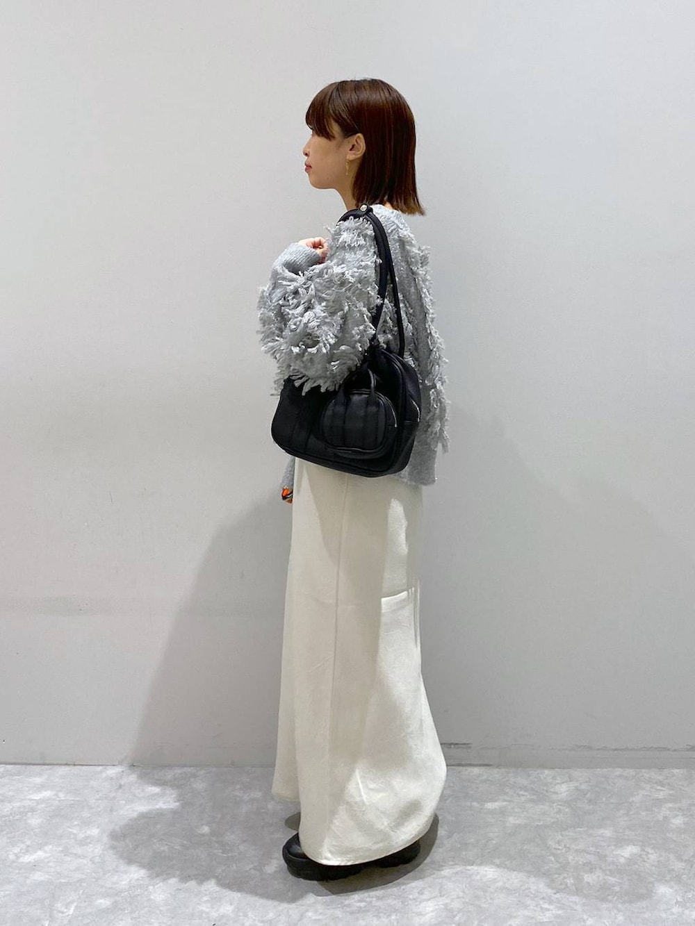 ブラック系のスニーカー、ホワイト系のスカート、グレー系のカーディガン/ボレロを着用したレディースの秋コーディネートの3枚目の写真