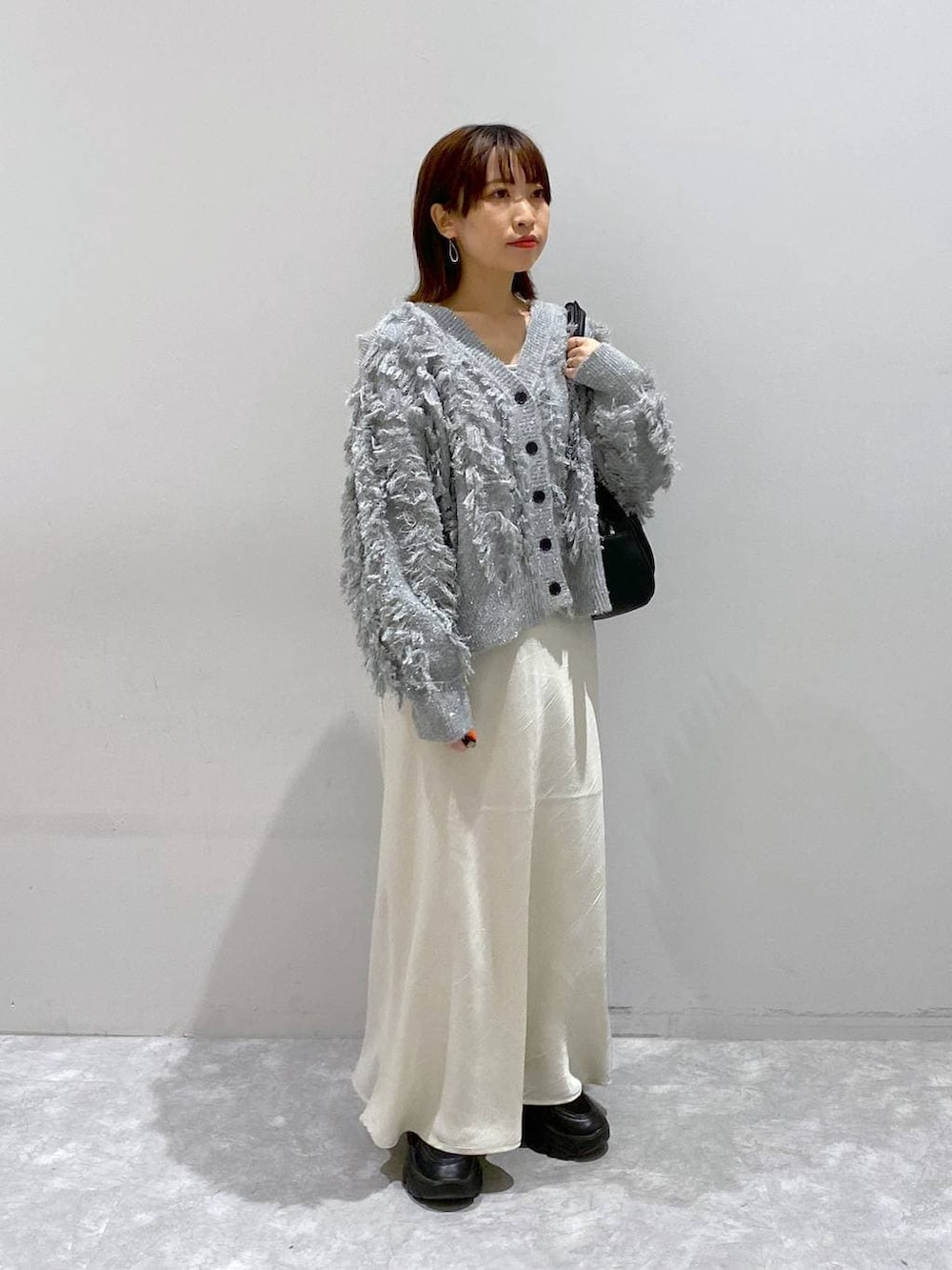 ブラック系のスニーカー、ホワイト系のスカート、グレー系のカーディガン/ボレロを着用したレディースの秋コーディネートの7枚目の写真