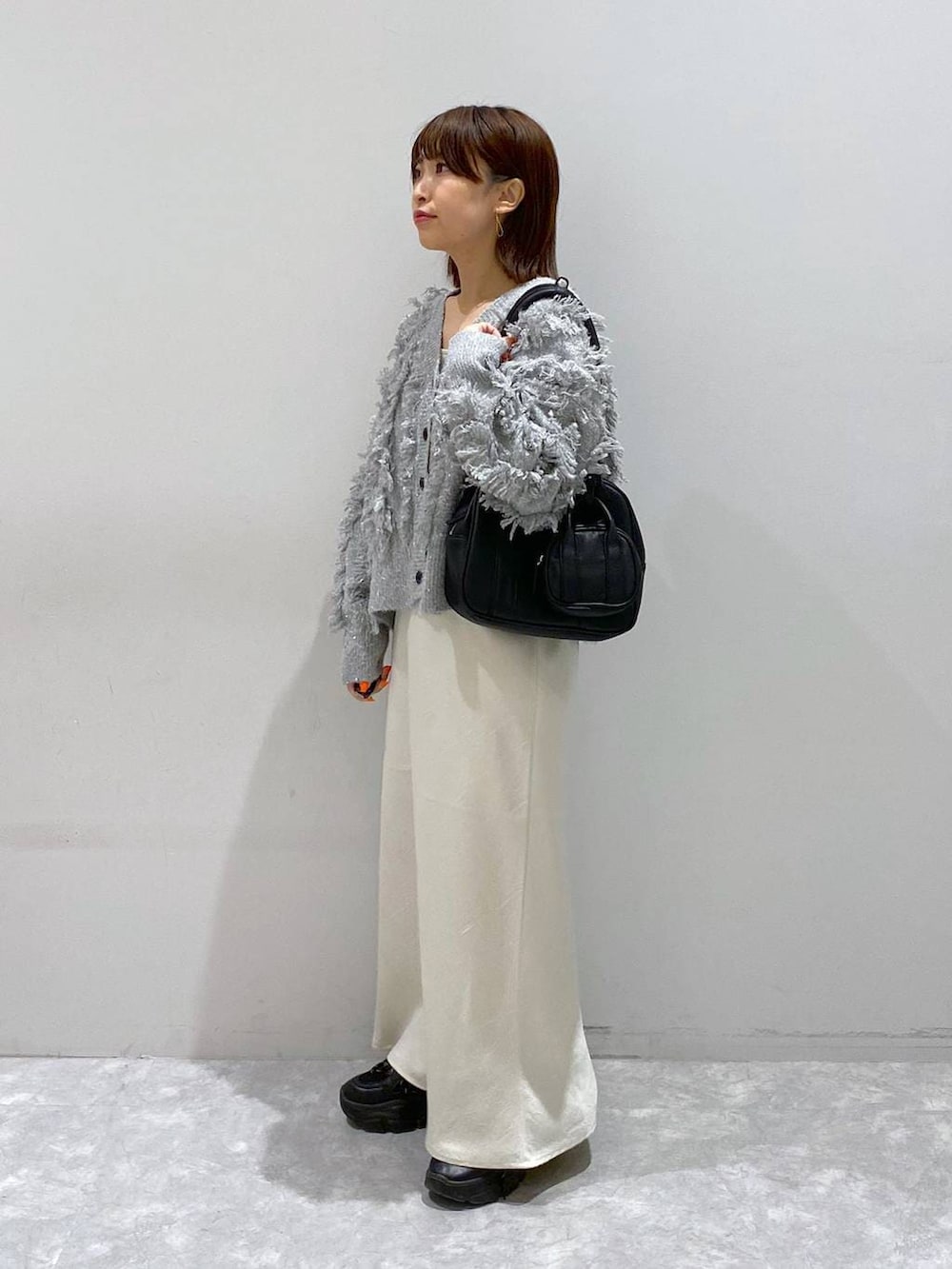 ブラック系のスニーカー、ホワイト系のスカート、グレー系のカーディガン/ボレロを着用したレディースの秋コーディネートの2枚目の写真