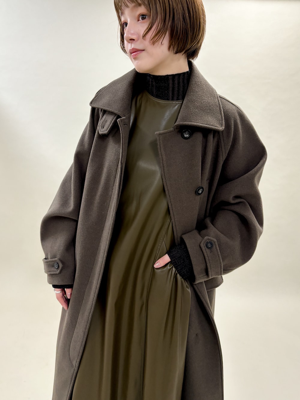 ブラウン系のステンカラーコート、ブラック系のニット/セーター、ブラウン系のワンピースを着用したレディースの冬コーディネートの3枚目の写真