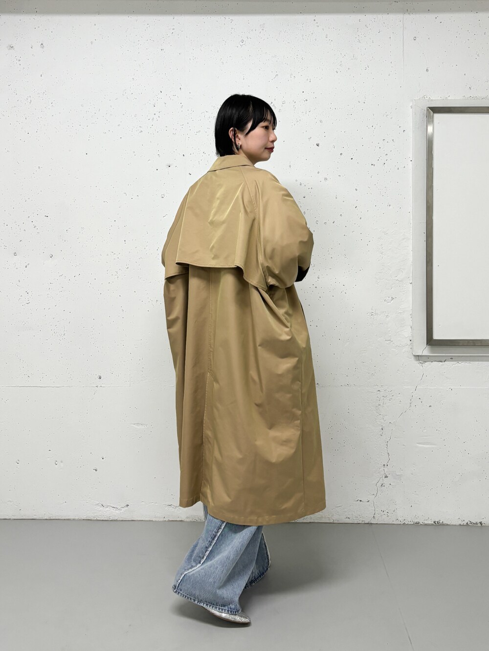 ベージュ系のステンカラーコート、グリーン系のシャツ/ブラウス、ブルー系のデニムパンツを着用したレディースの春コーディネートの2枚目の写真