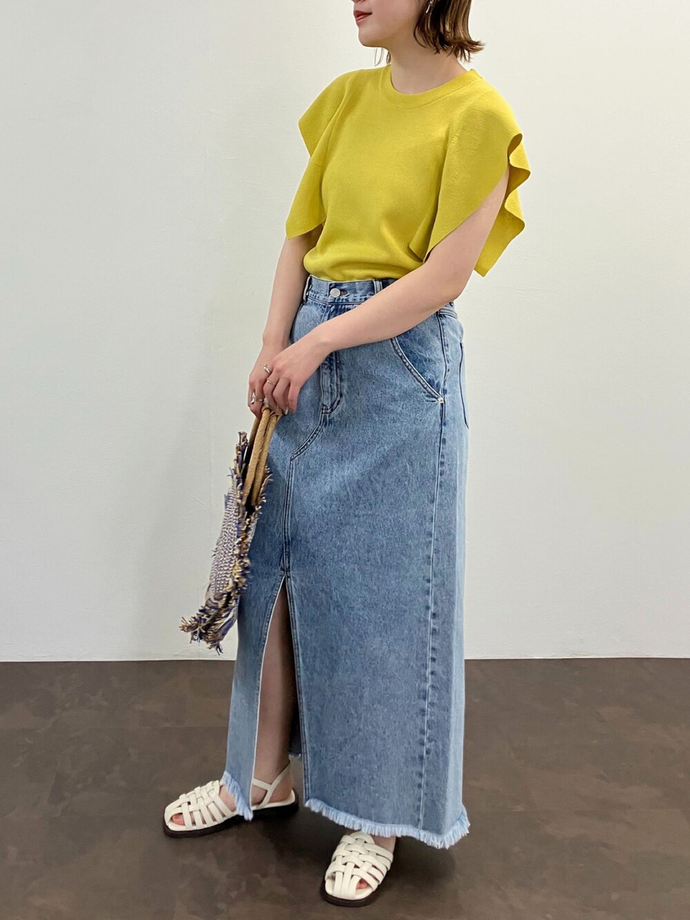 イエロー系のニット/セーター、ブルー系のスカート、ホワイト系のサンダルを着用したレディースの春コーディネートの2枚目の写真