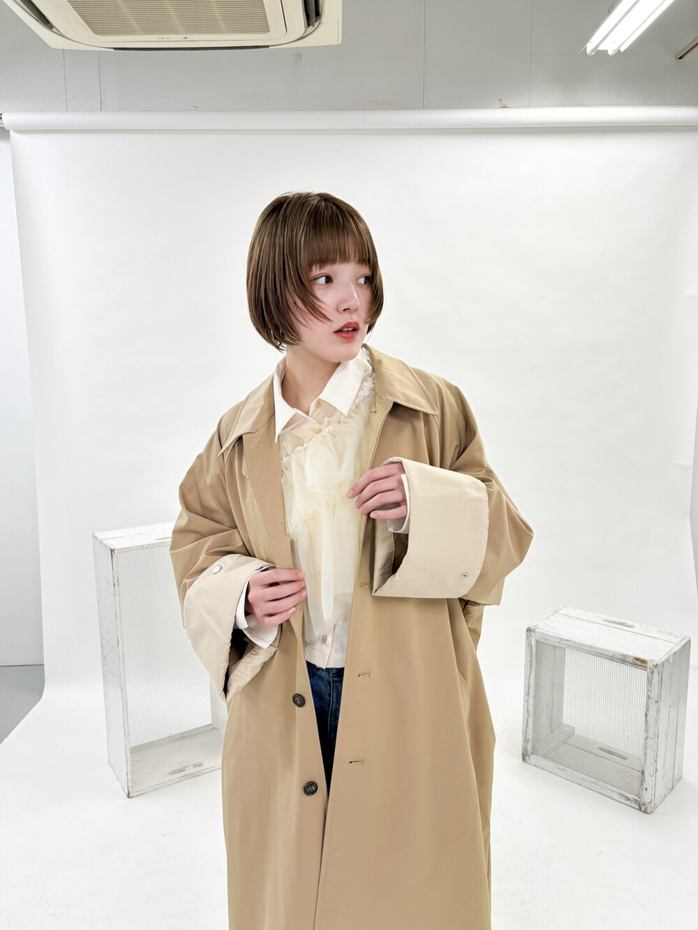 ベージュ系のステンカラーコート、ホワイト系のシャツ/ブラウス、ブルー系のデニムパンツを着用したレディースの冬コーディネートの3枚目の写真