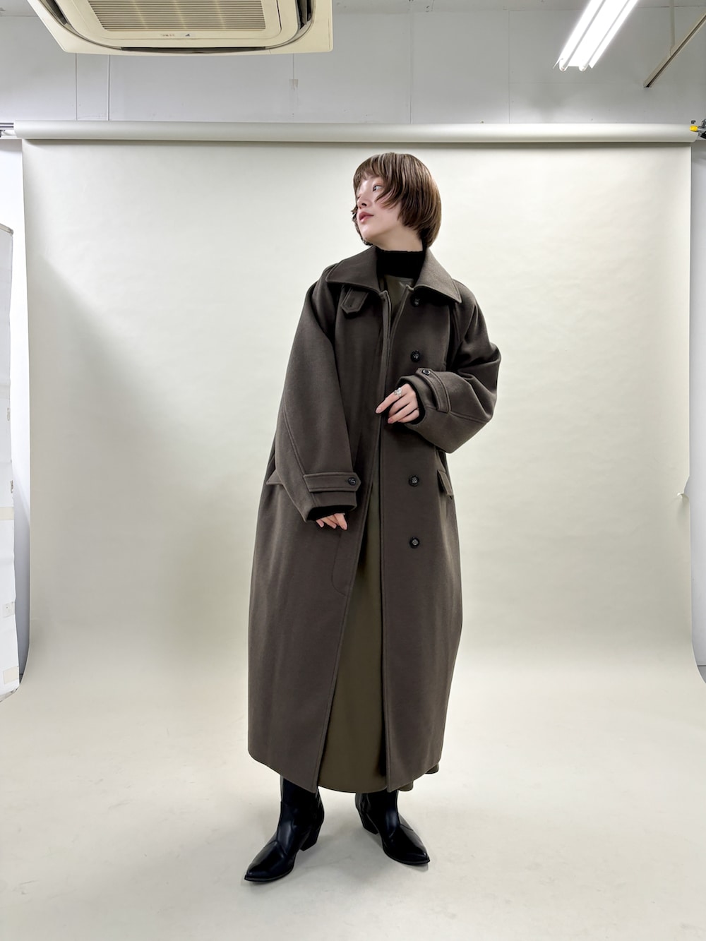 ブラウン系のステンカラーコート、ブラック系のニット/セーター、ブラウン系のワンピースを着用したレディースの冬コーディネートの2枚目の写真