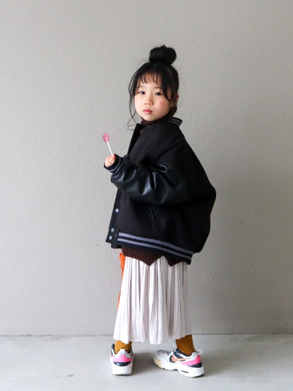 ブラック系のスタジャン、ブラウン系のニット/セーター、ホワイト系のスカートを着用したキッズの冬コーディネートの4枚目の写真