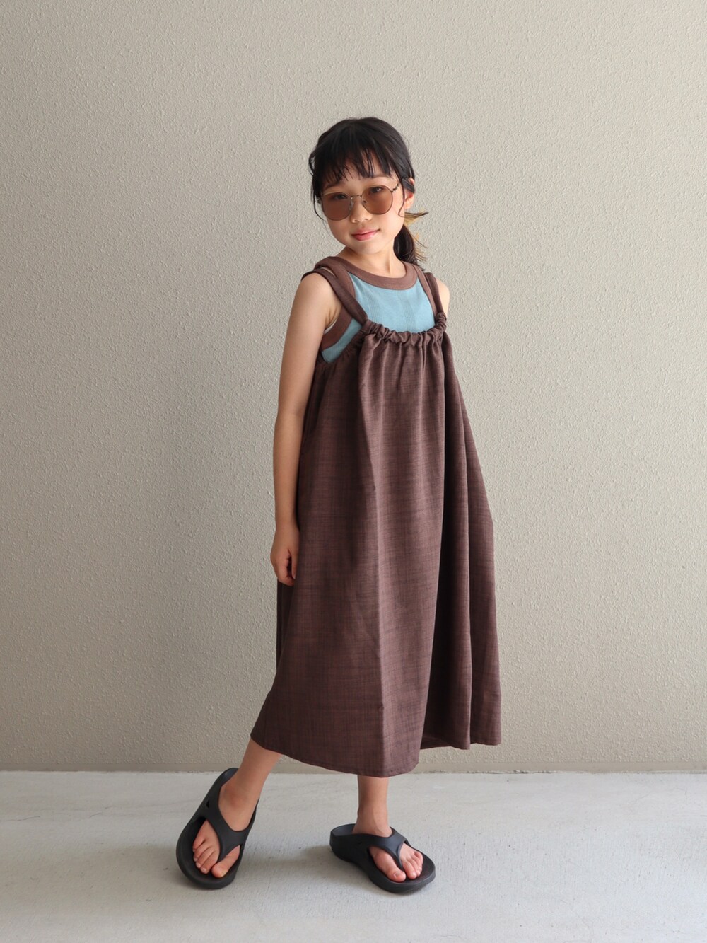 ブラウン系のワンピース、ブラック系のサンダル、ブルー系のタンクトップを着用したキッズの夏コーディネートの4枚目の写真