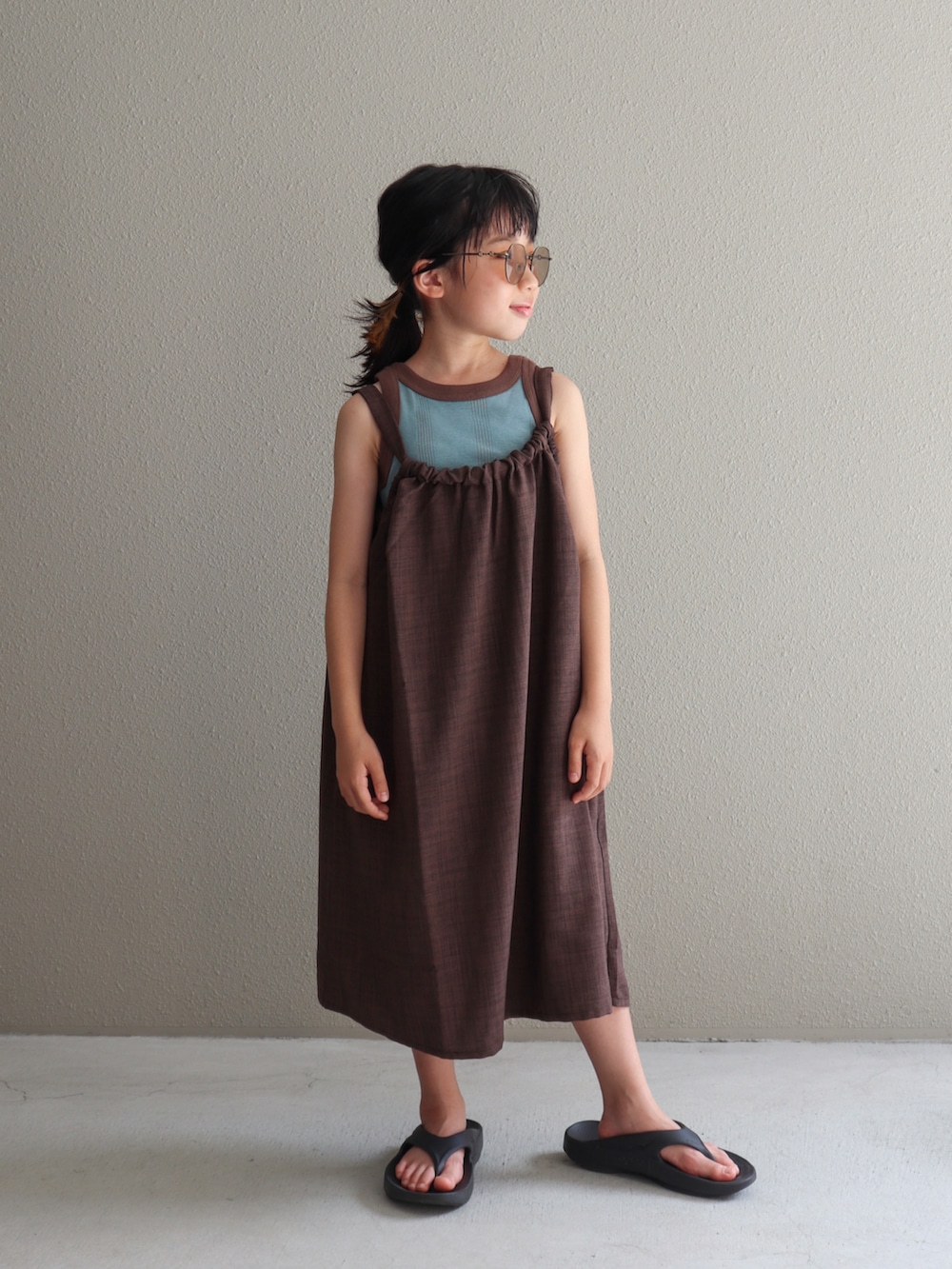 ブラウン系のワンピース、ブラック系のサンダル、ブルー系のタンクトップを着用したキッズの夏コーディネートの3枚目の写真