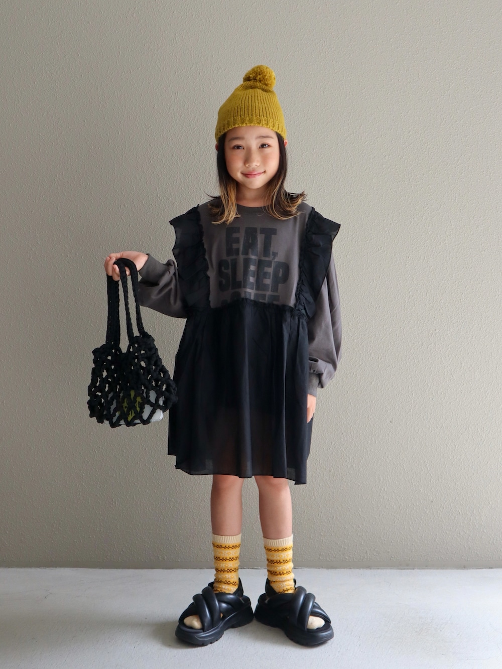 ブラック系のスカート、グレー系のワンピース、ブラック系のサンダルを着用したキッズの秋コーディネートの2枚目の写真