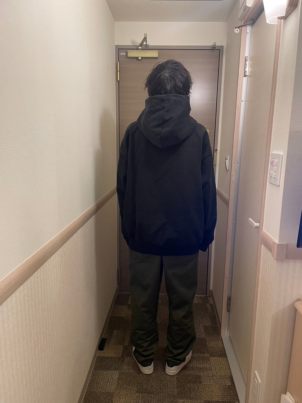 グリーン系のチノパンツ、ホワイト系のスニーカー、ブラック系のパーカーを着用したメンズの冬コーディネートの2枚目の写真