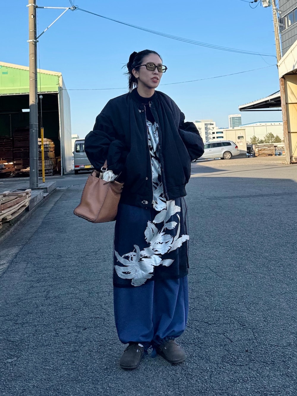 ブラック系のブルゾン、ブルー系のスウェットパンツ、ブラウン系のハンドバッグを着用したレディースの冬コーディネートの2枚目の写真