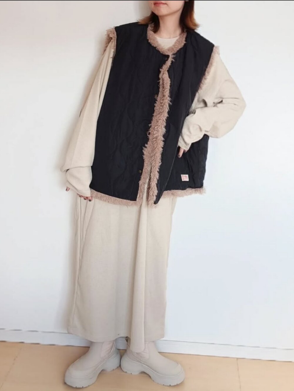 ブラック系のベスト、ベージュ系のワンピース、ベージュ系のブーツを着用したレディースの冬コーディネートの2枚目の写真