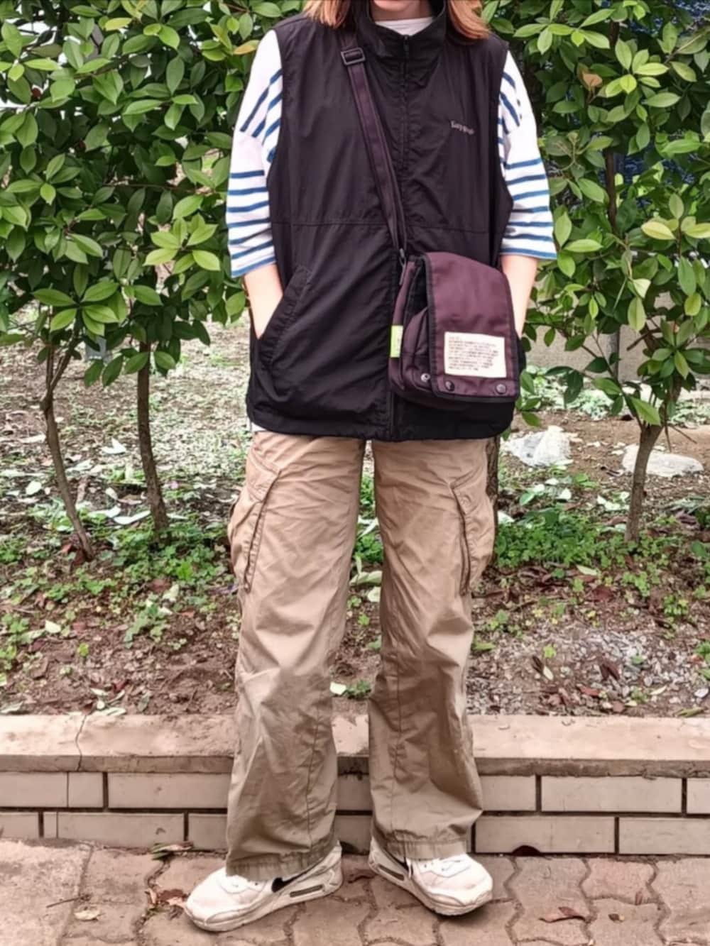 ブラック系のベスト、ブルー系のTシャツ/カットソー、ブラック系のショルダーバッグを着用したレディースの春コーディネートの2枚目の写真