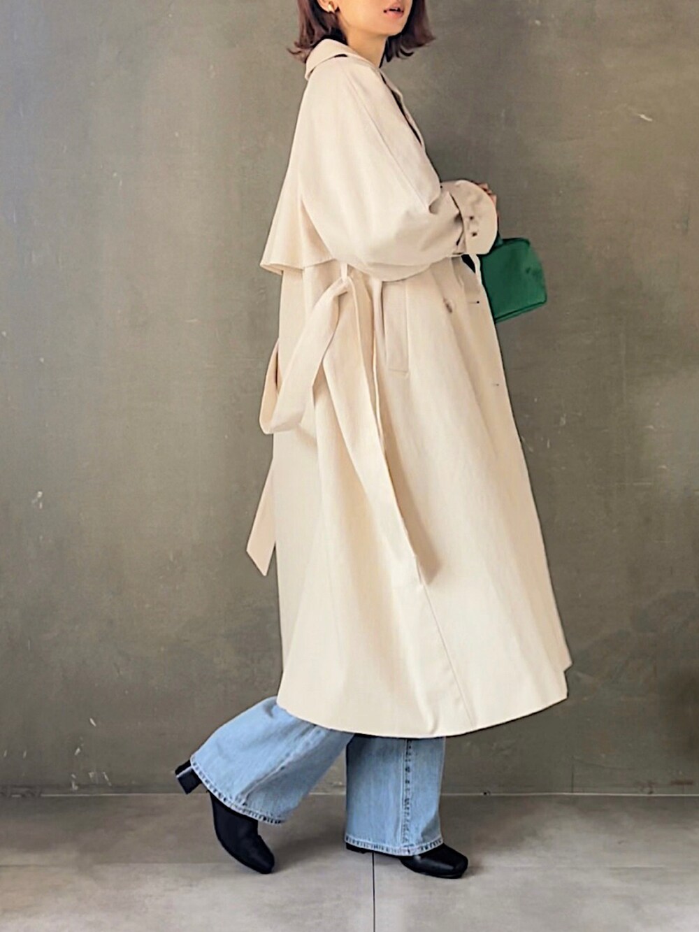 ホワイト系のトレンチコート、ブラック系のスウェット、ブルー系のデニムパンツを着用したレディースの春コーディネートの2枚目の写真