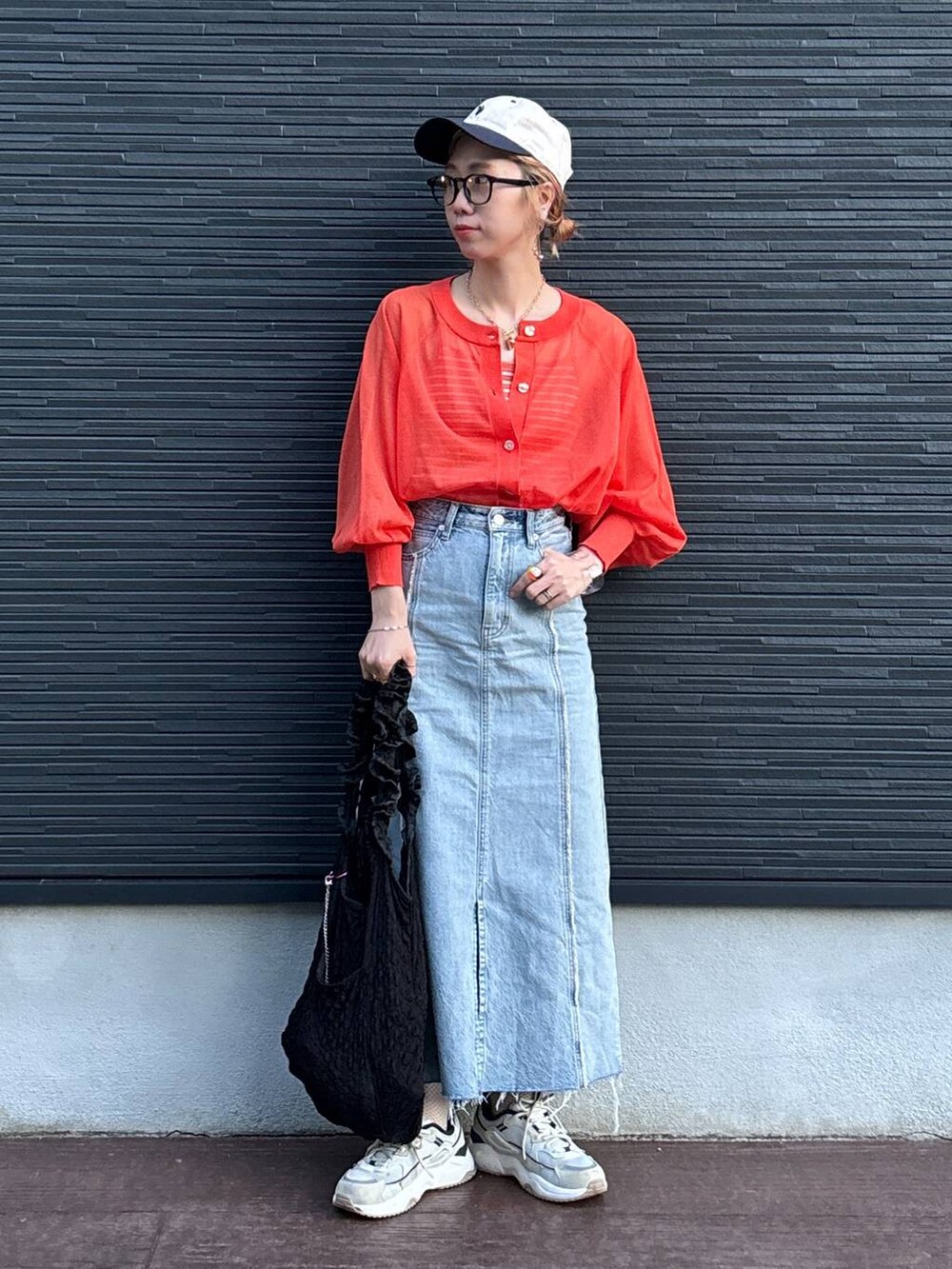 ブラック系のトートバッグ、オレンジ系のカーディガン/ボレロ、ブルー系のスカートを着用したレディースの夏コーディネートの2枚目の写真