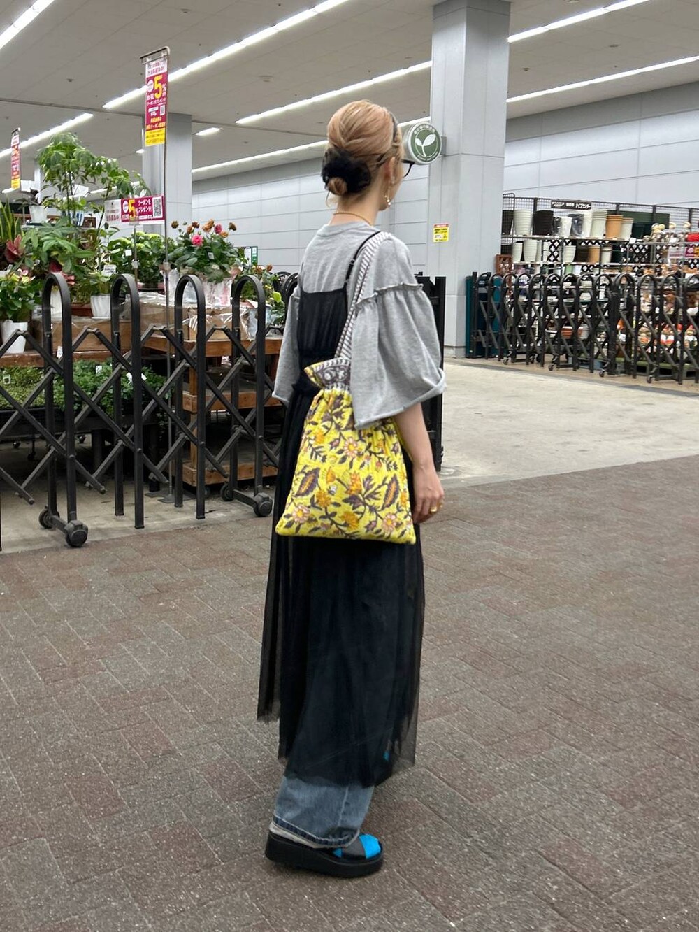 ブラック系のサンダル、ブルー系のデニムパンツ、イエロー系のトートバッグを着用したレディースの春コーディネートの3枚目の写真