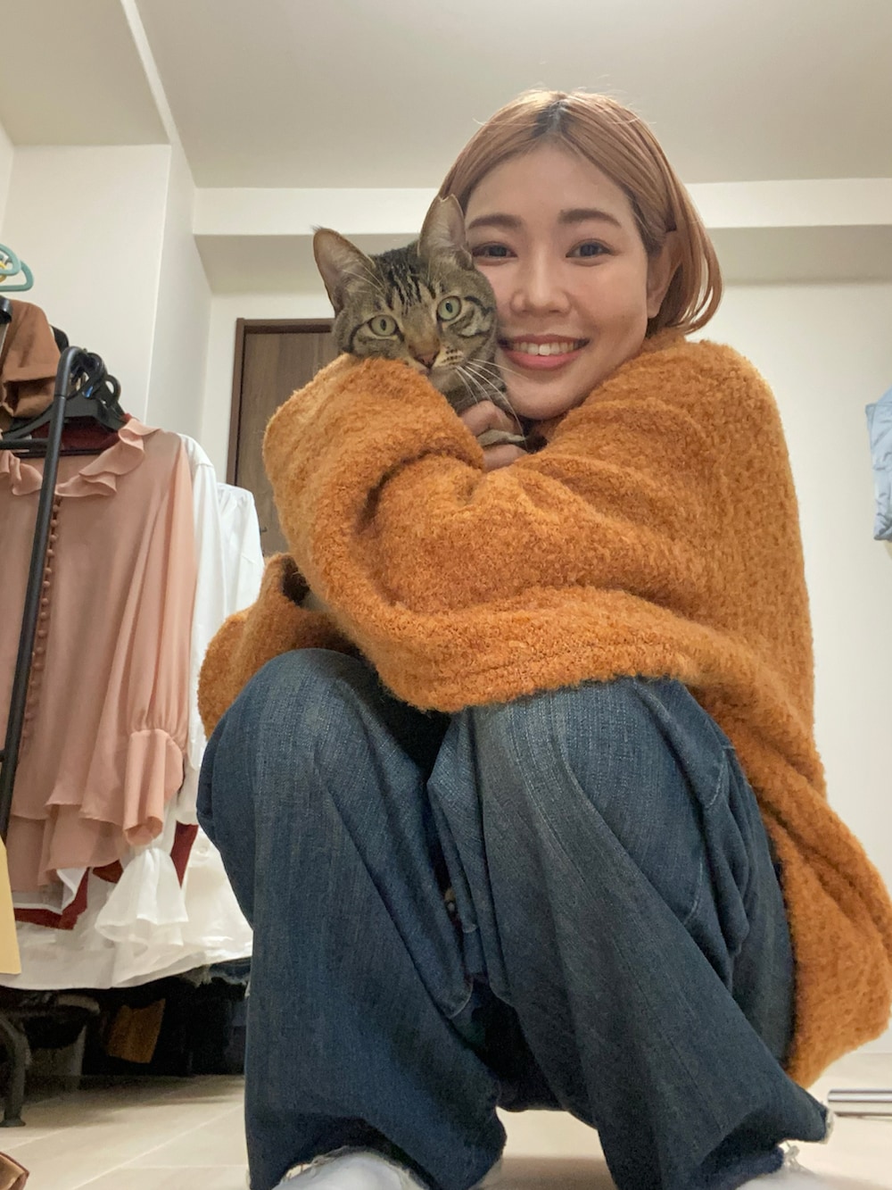 オレンジ系のニット/セーター、ホワイト系のニット/セーター、ブルー系のデニムパンツを着用したレディースの冬コーディネートの2枚目の写真