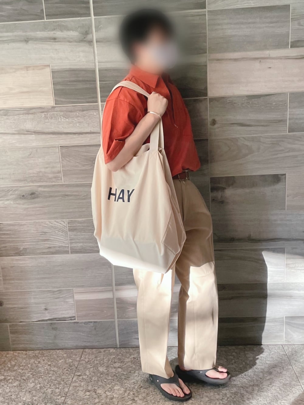 レッド系のTシャツ/カットソー、ベージュ系のチノパンツ、ホワイト系のトートバッグを着用したメンズの夏コーディネートの3枚目の写真