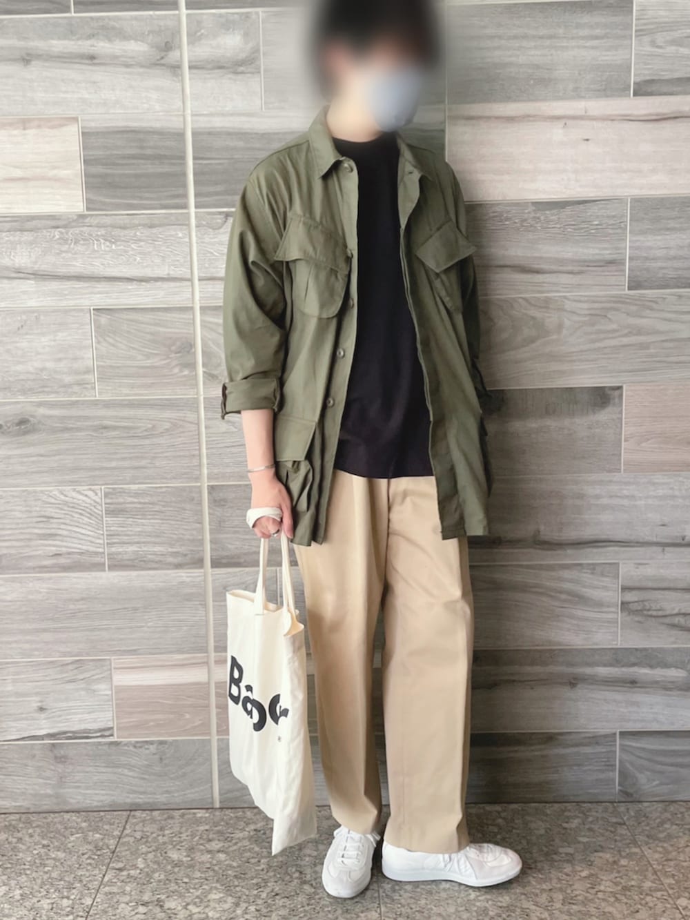 グリーン系のミリタリージャケット、ブラック系のTシャツ/カットソー、ベージュ系のチノパンツを着用したメンズの春コーディネートの2枚目の写真